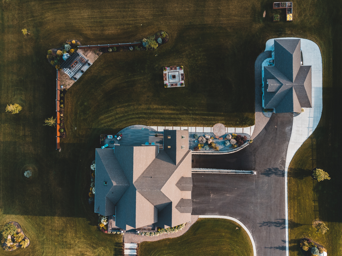 Aerial of a large home and guest house with dark shingle roofs and a pool