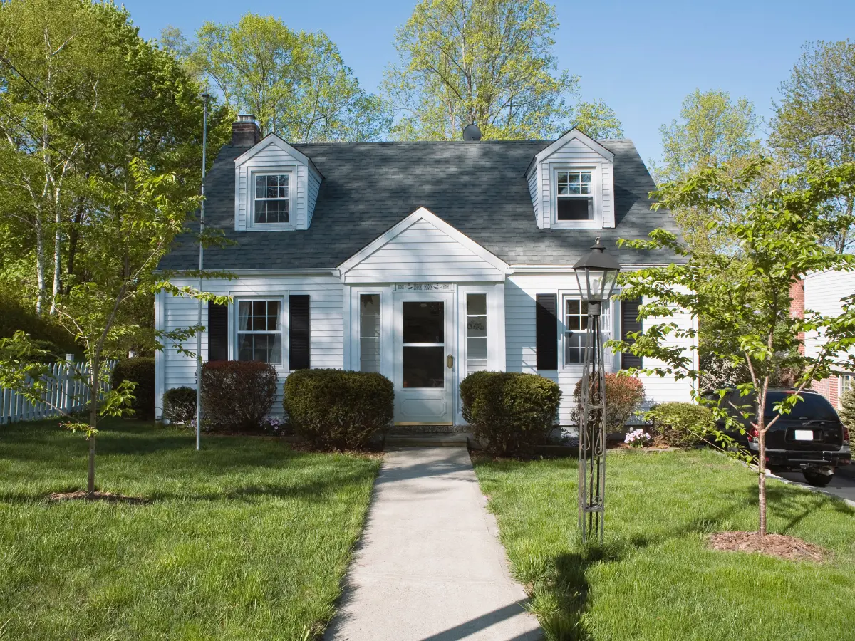 White Cape Cod home with two dormers and a dark gray shingle roof