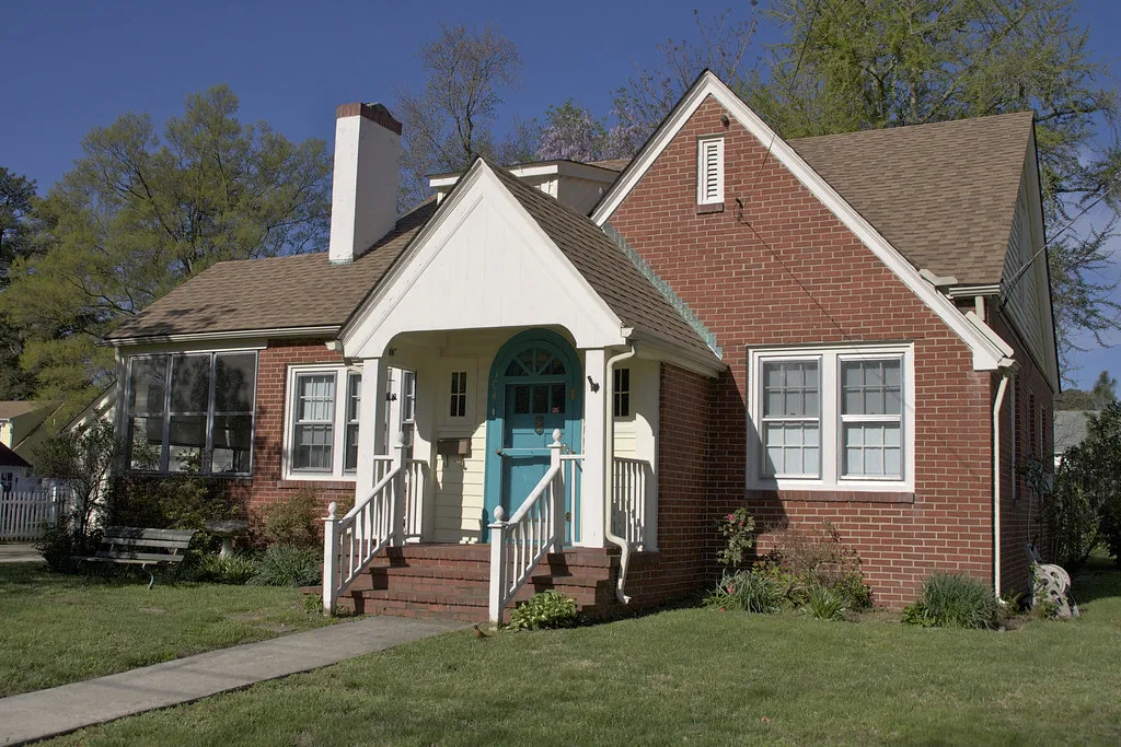Brick home with a white chimney and asphalt shingle roof on a sunny day