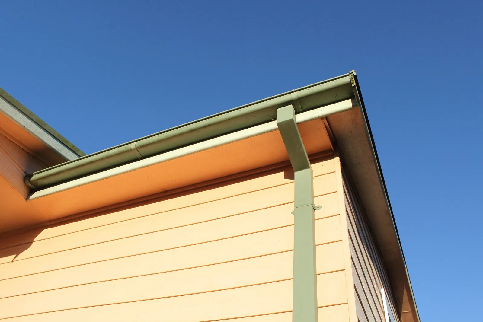 Metal rain gutter and downspout running along the roof edge of a house