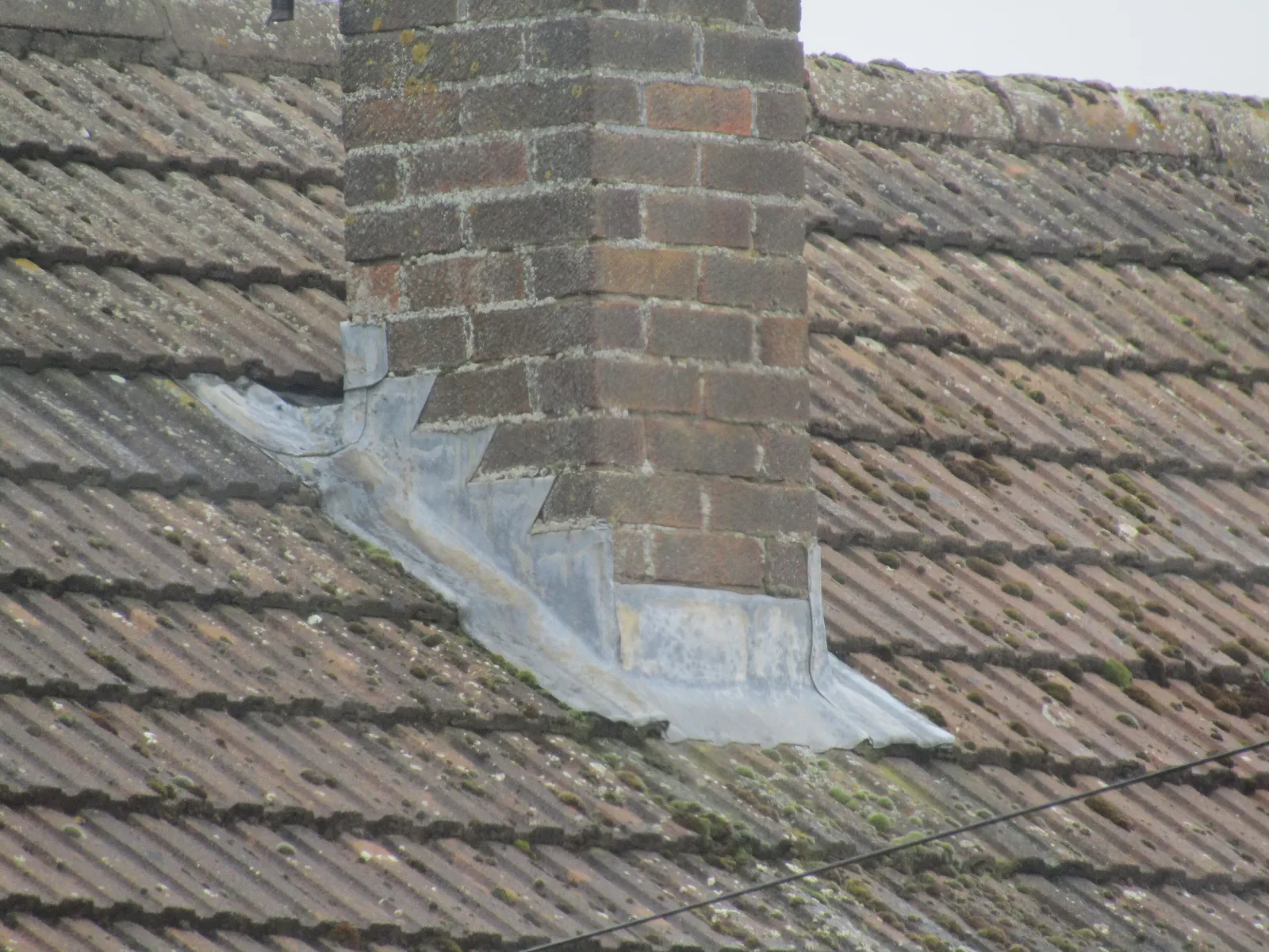 Lead flashing sealed around a brick chimney on a shingle roof
